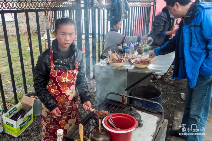 川西塔公草原木雅金頂前的廣場(chǎng)上，一位藏族小姑娘利用雙休日，幫助家人在這里賣烤肉串。