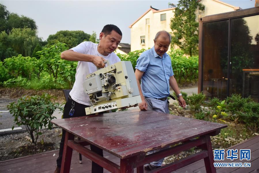 　6月30日，朱生榮（右）和兒子朱強(qiáng)（左）在馬鳴村將軍湖廣場(chǎng)布置放映設(shè)備。在浙江嘉興桐鄉(xiāng)市洲泉鎮(zhèn)馬鳴村，王志華、朱文炳、朱生榮、朱強(qiáng)四代電影放映員，“接力”放映電影五十余年。一臺(tái)放映機(jī)、幾盤(pán)膠片、一面白墻，構(gòu)成他們的“流動(dòng)電影院”，“噠噠”的走帶聲轉(zhuǎn)出了光影老味道，也轉(zhuǎn)動(dòng)了整村人的文化生活。 第四代放映人“85后”小伙朱強(qiáng)從小在幕布前長(zhǎng)大，深受父輩影響。隨著數(shù)字電影的普及，膠片電影逐漸退場(chǎng)。如今的他在馬鳴電影館、學(xué)校等場(chǎng)所進(jìn)行教學(xué)、展示等活動(dòng)，宣傳電影文化。對(duì)他而言，一代接一代從事電影工作，就是為了承續(xù)傳統(tǒng)。“師爺爺教我們認(rèn)真放好每部電影，即便只有一位觀眾，我們也不會(huì)讓它停機(jī)?！敝鞆?qiáng)說(shuō)。新華社記者 鄭夢(mèng)雨 攝