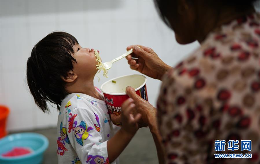 7月9日，村民在給小朋友喂飯。 當日，江西鄱陽縣鄱陽鎮(zhèn)因洪水受災的村民被轉(zhuǎn)移到多個集中安置點。在鄱陽縣五一中心學校安置點，志愿者和工作人員接到任務后不到十小時內(nèi)，為被轉(zhuǎn)移村民布置了28間教室，供519人安頓，并為村民發(fā)放褥子、床單、枕頭、盒飯、飲用水等物資。 新華社記者 周密 攝