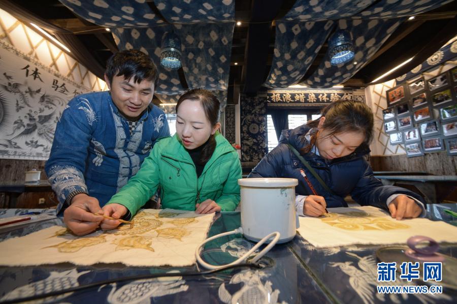 12月1日，在丹寨縣金泉街道千年傳蠟染制作坊，王方周（左）在指導(dǎo)游客畫蠟畫。今年40歲的王方周是貴州省黔東南苗族侗族自治州丹寨縣排調(diào)鎮(zhèn)排聳村人，自幼喜歡繪畫和書法，對(duì)傳統(tǒng)蠟染制作手工藝也有著濃厚興趣。2016年8月，在外打工的王方周返鄉(xiāng)與人合作創(chuàng)辦了千年傳蠟染制作坊。后來，他們又在丹寨萬達(dá)旅游小鎮(zhèn)開辦歐報(bào)浪蠟染體驗(yàn)館。蠟染制作坊和蠟染體驗(yàn)館在今年已接待游客6000多名，創(chuàng)收30多萬元，也為當(dāng)?shù)匾椎胤鲐毎徇w安置點(diǎn)的13名村民提供月收入在2000元左右的就業(yè)崗位。王方周說，帶動(dòng)更多的群眾增收致富，傳承傳統(tǒng)手工藝，這就是我們創(chuàng)辦蠟染制作坊的初衷。新華社記者 楊楹 攝